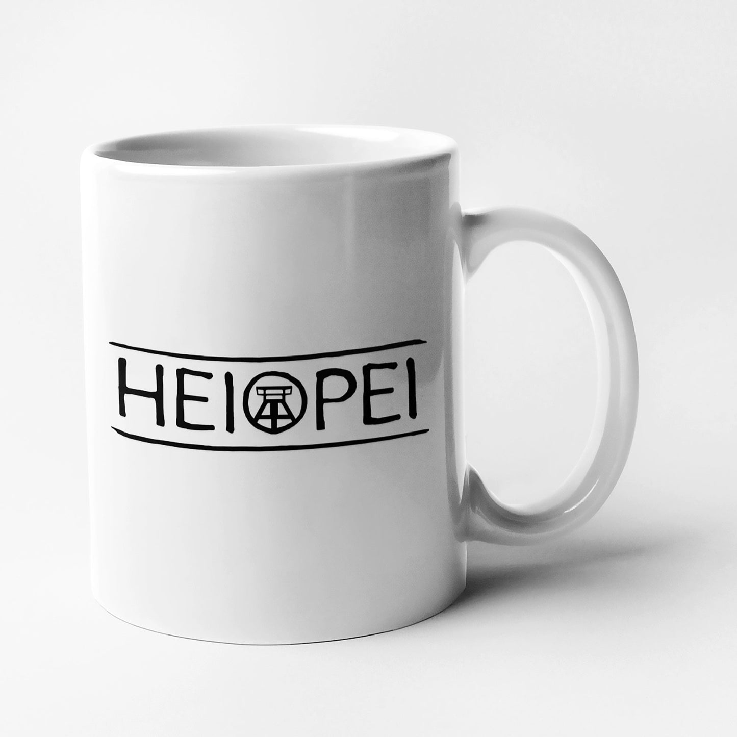 Weiße Keramiktasse mit schwarzem Ruhrpott-Spruch 'Heiopei', beidseitig bedruckt.