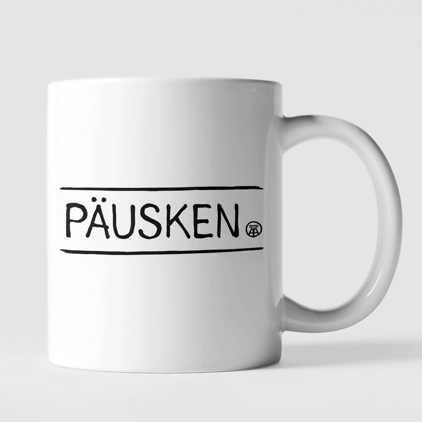 Weiße Keramiktasse mit schwarzem 'PÄUSKEN'-Schriftzug, ideal für Kaffeepausen.