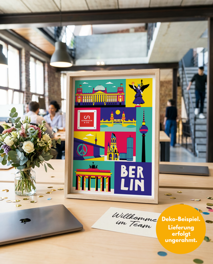 Geschenk Onboarding: Berlin Kunstdruck mit integriertem Firmenlogo auf einem Holzschreibtisch im modernen Großraumbüro, daneben Blumen, Konfetti und eine Grußkarte mit der Aufschrift "Willkommen im Team".