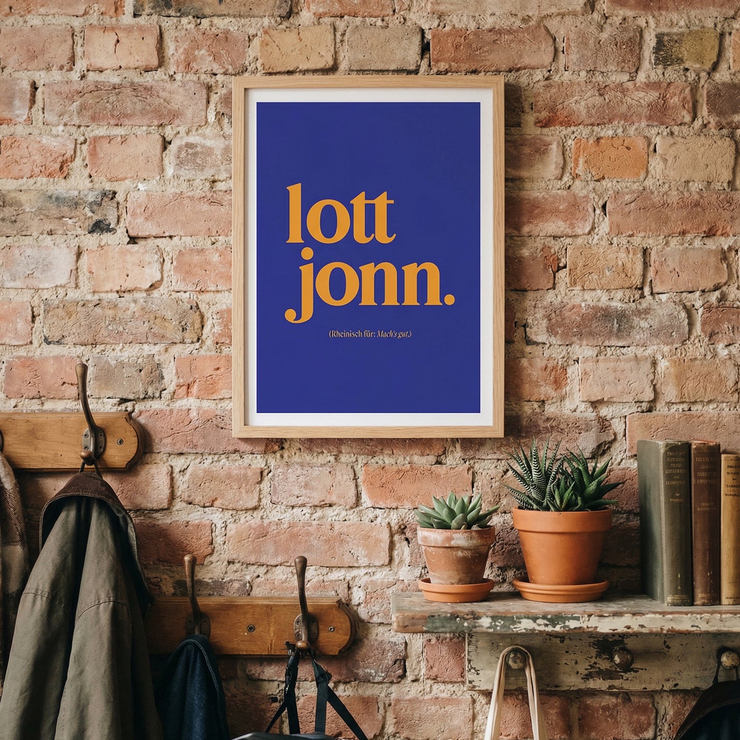 Blau-oranges Typografie-Poster „lott jonn.“ in A3 im Holzrahmen, stilvoll inszeniert an einer Backsteinwand im Flur mit Garderobe, Pflanzen und Büchern