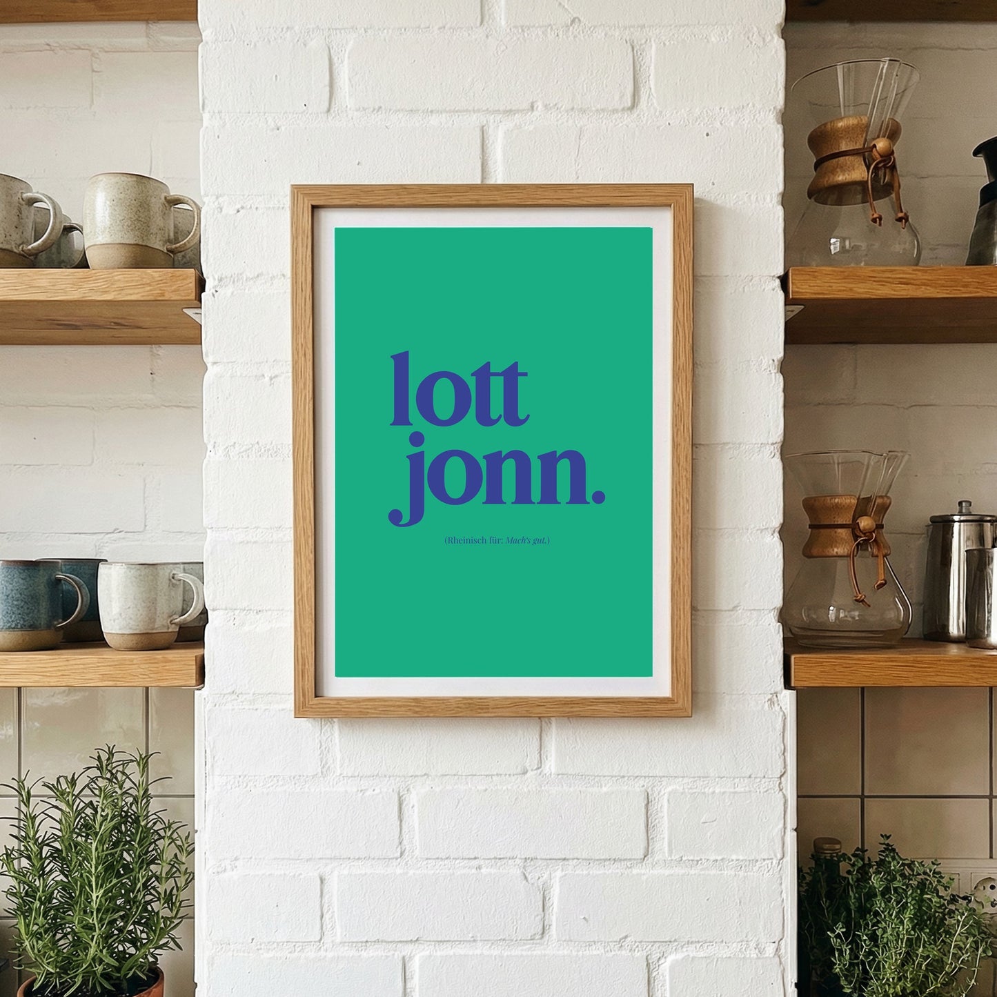 Türkisfarbenes Poster mit dem rheinischen Spruch „lott jonn.“ in A3, gerahmt und dekorativ platziert an einer weißen Ziegelwand in moderner Küche mit Kräutern und Keramik