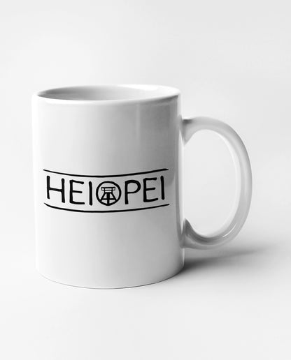 Weiße Keramiktasse mit schwarzem Ruhrpott-Spruch 'Heiopei', beidseitig bedruckt.