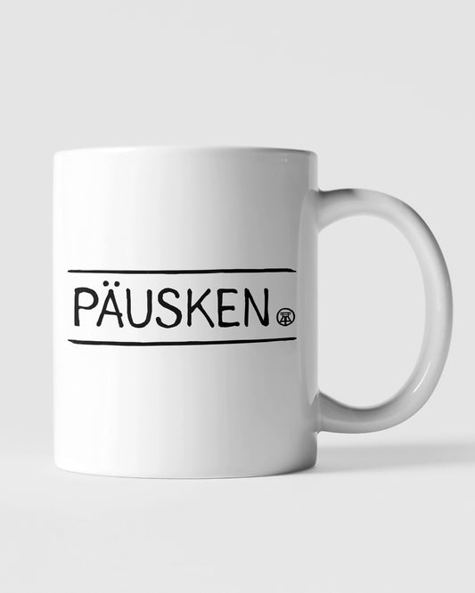 Weiße Keramiktasse mit schwarzem 'PÄUSKEN'-Schriftzug, ideal für Kaffeepausen.