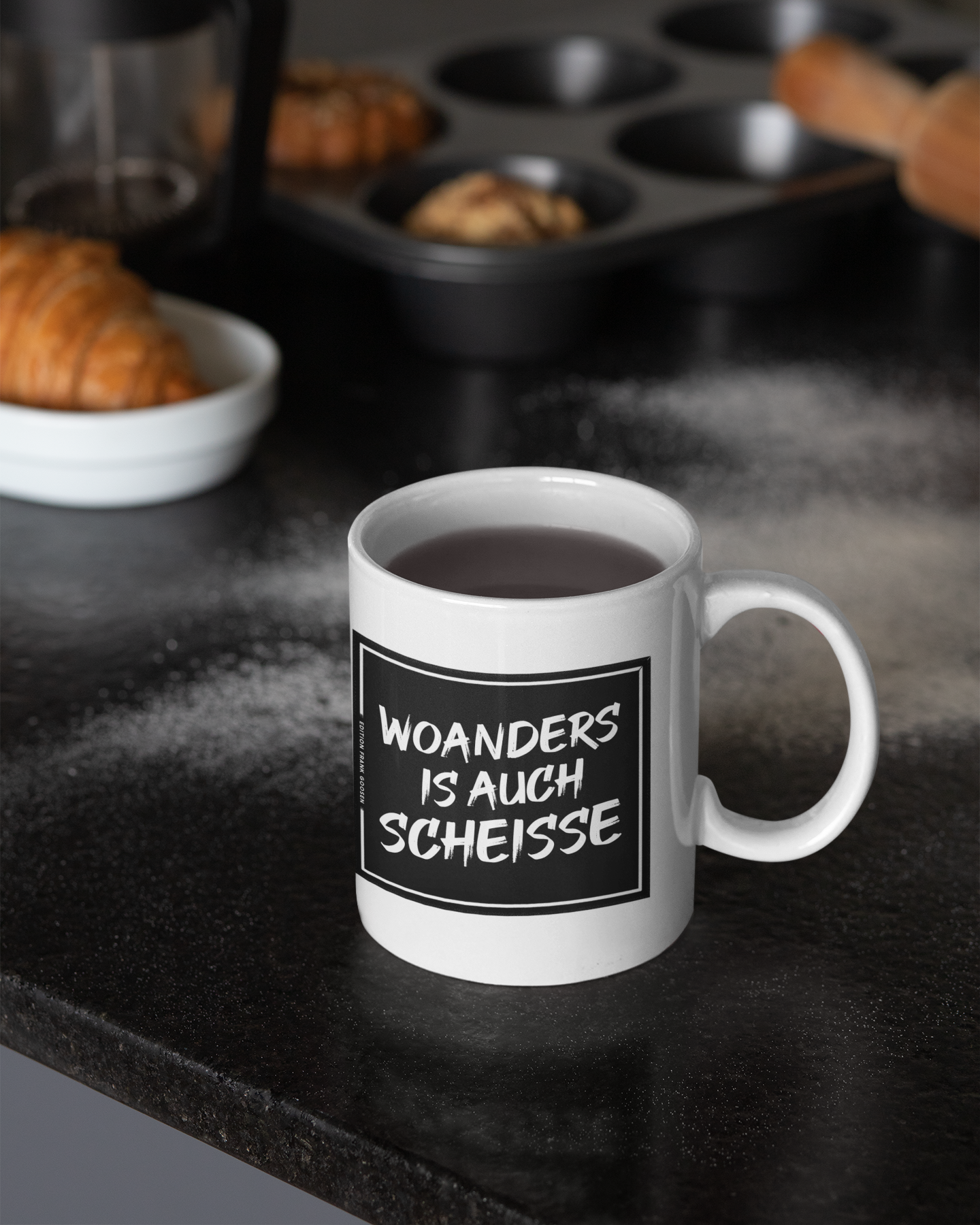 Weiße Kaffeetasse mit schwarzem Schriftzug 'Woanders is auch scheiße' – perfekte Geschenkidee für Ruhrpott-Liebhaber.